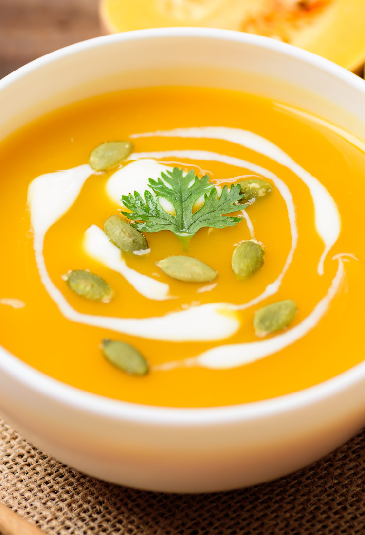 Bowl of creamy vegan butternut squash soup topped with pumpkin seeds and a swirl of coconut milk