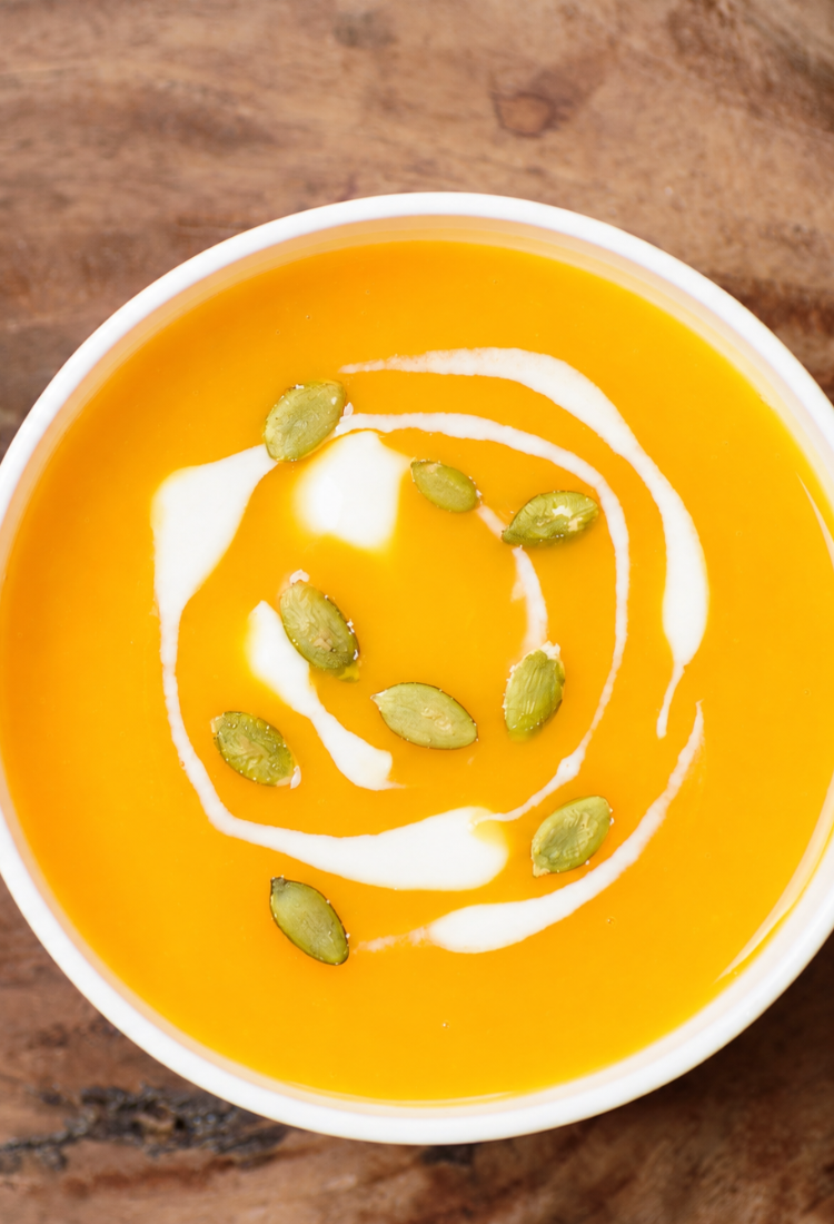 Roasted butternut squash soup in a white bowl with pepitas and a drizzle of coconut milk
