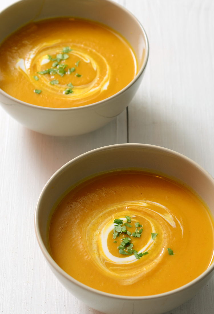 Two bowls of dairy-free butternut squash soup with coconut milk swirls and pepitas on a table