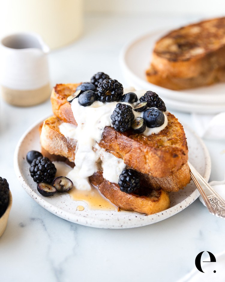 Two slices of vegan French toast stacked on a plate with coconut whipped cream and fresh berries