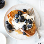 Overhead view of vegan French toast with coconut whipped cream, blackberries, blueberries and maple syrup on a speckled plate