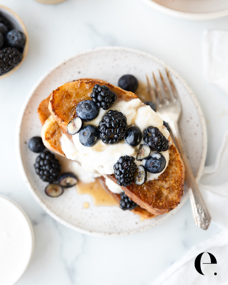 Overhead view of vegan French toast with coconut whipped cream, blackberries, blueberries and maple syrup on a speckled plate