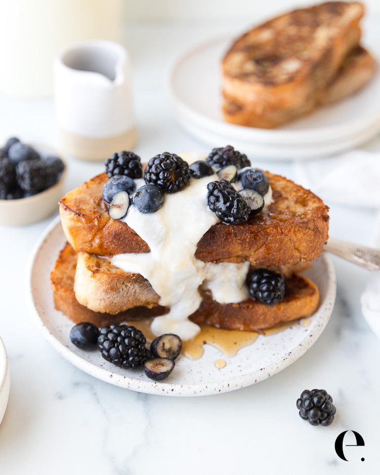 Stack of vegan French toast topped with coconut whipped cream, blackberries, blueberries and maple syrup