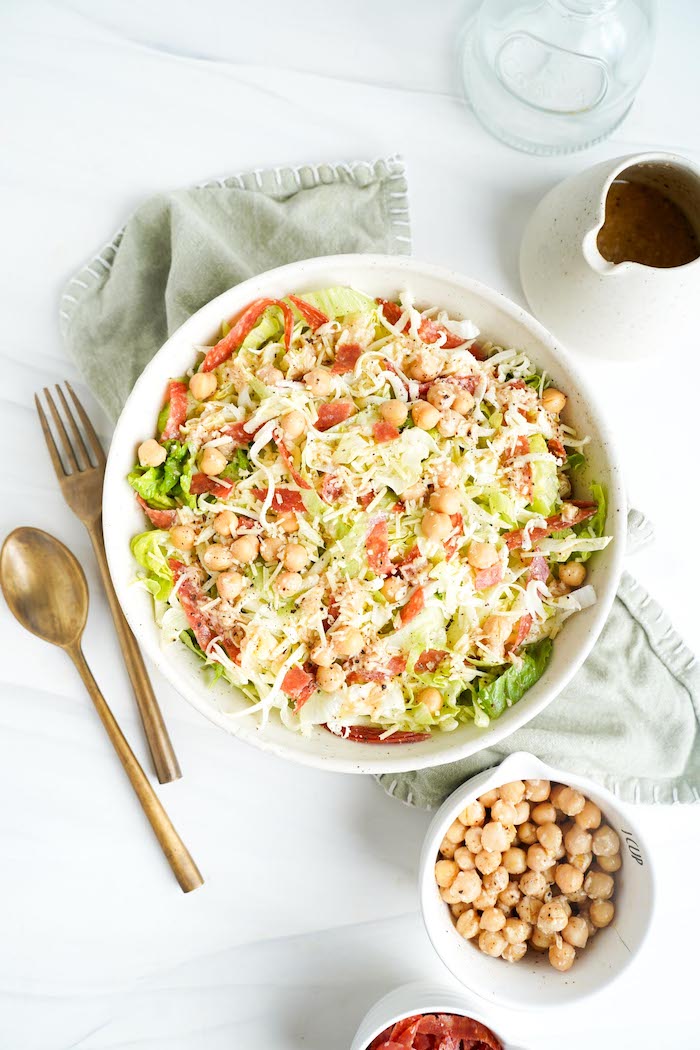 La Scala chopped salad in a white bowl with shredded iceberg and romaine, salami, mozzarella and marinated chickpeas, next to a pitcher of dressing