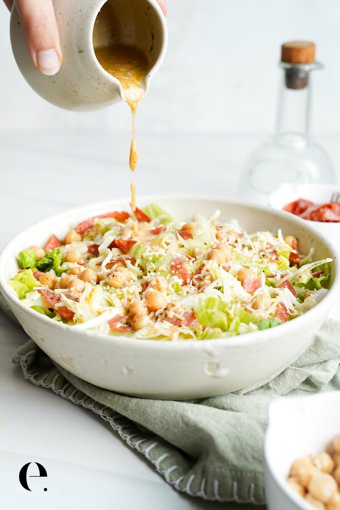 Pouring Dijon Parmesan dressing over a homemade La Scala chopped salad