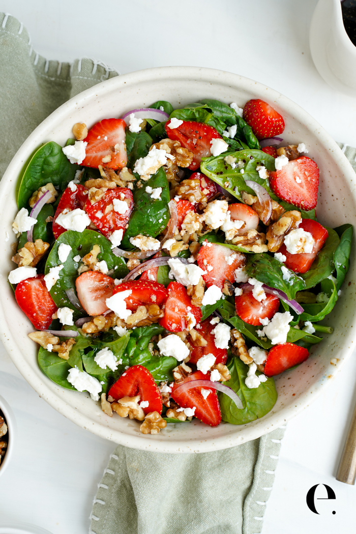 Strawberry spinach salad with sliced strawberries, goat cheese crumbles and chopped walnuts in a white bowl