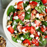 Overhead view of strawberry spinach salad with goat cheese and walnuts, with small bowls of walnuts and strawberries on the side