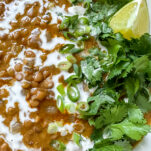 Bowl of red curry lentil soup garnished with fresh cilantro and lime wedges