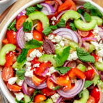 Greek salad made with tomato, cucumber, olives, red onion, mint, oregano, feta and olive oil in bowl.