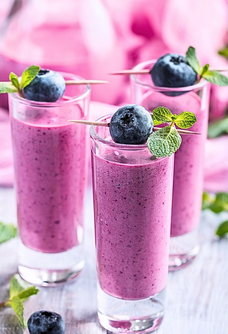Purple High-Fiber Breakfast Smoothie in three glasses with blueberries and mint garnish