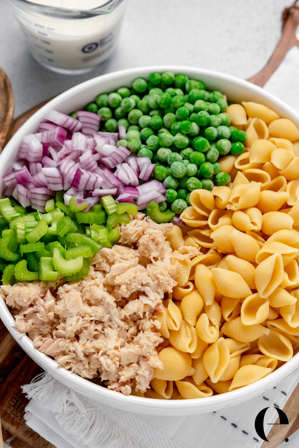 Easy tuna pasta salad ingredients in a bowl before mixing, including pasta, tuna, celery, red onion, and peas