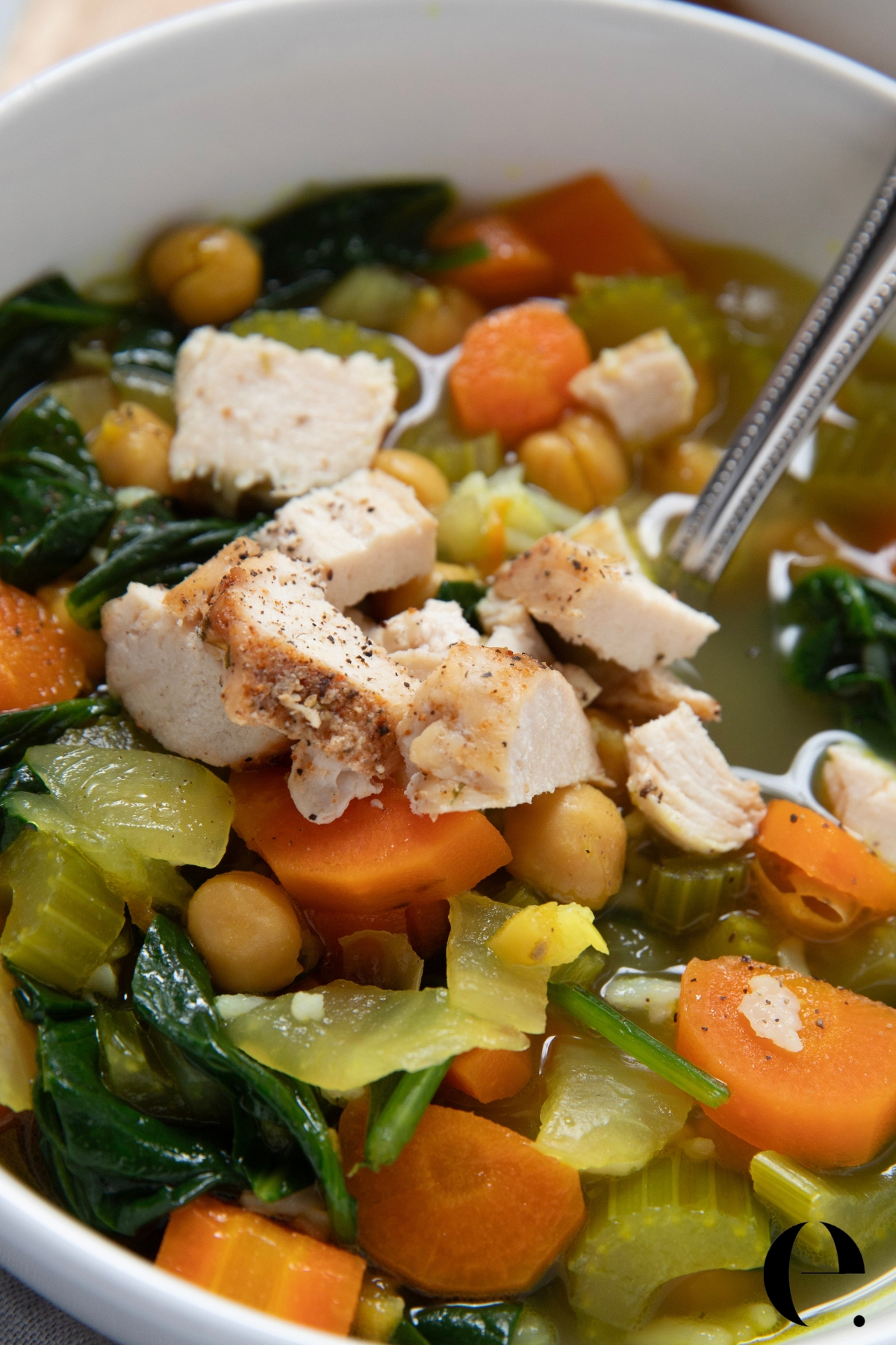 close up of Blue Zones longevity soup in a white bowl with turmeric broth, chickpeas, pasta, leafy greens, carrots, and shredded chicken, finished with fresh lemon and extra virgin olive oil