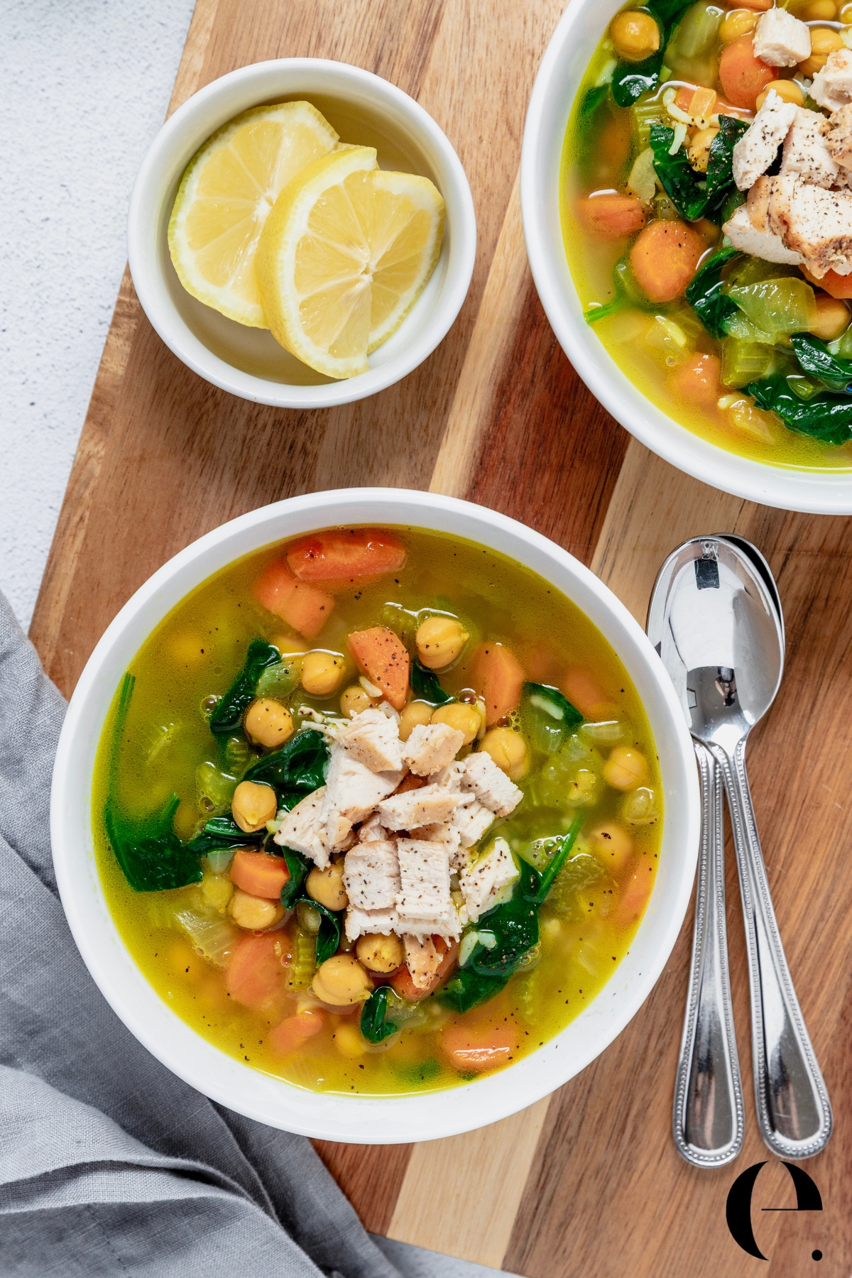 Blue Zones longevity soup in a white bowl with turmeric broth, chickpeas, pasta, spinach, carrots, and shredded chicken, finished with fresh lemon and olive oil