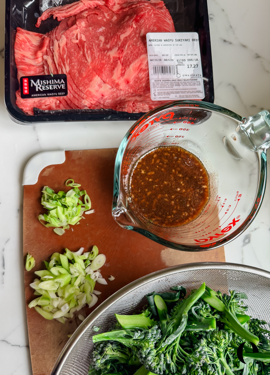 Prepped ingredients including sliced beef, chopped green onions, whisked umami sauce, and chopped broccolini