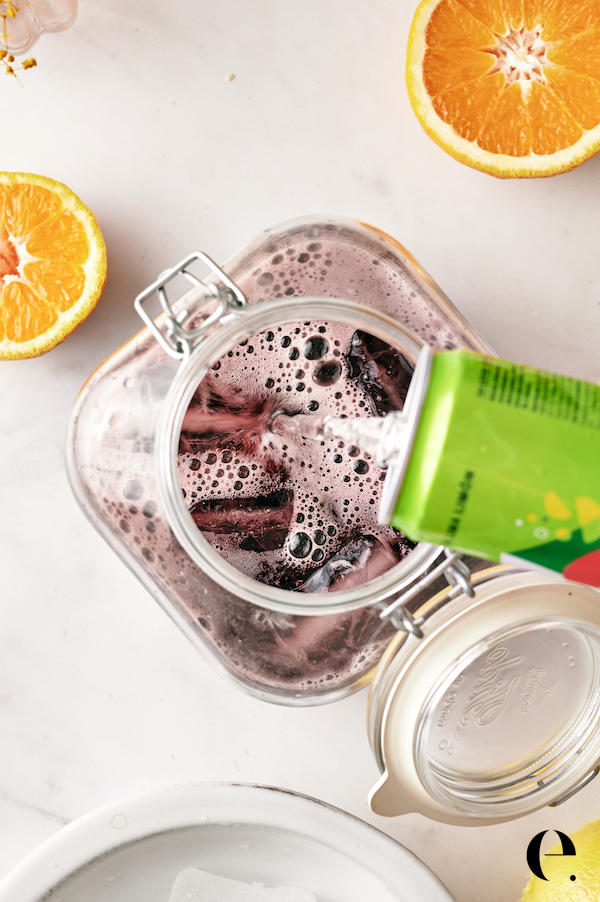 Topping the pitcher of red wine with lemon-lime soda and orange slices