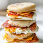 Turkey Bacon Breakfast Sandwiches stacked on plate with egg, cheese, english muffin, turkey bacon and chives
