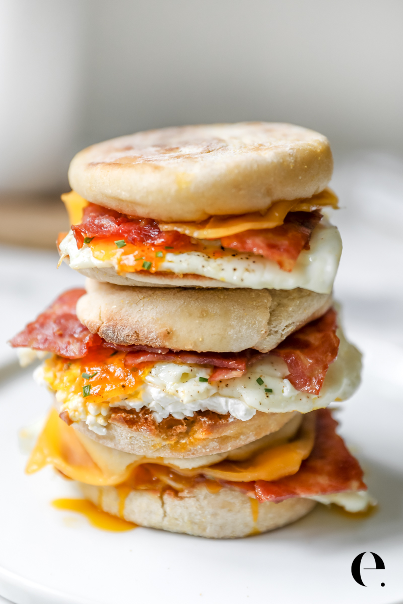 Turkey Bacon Breakfast Sandwiches stacked on plate with egg, cheese, english muffin, turkey bacon and chives