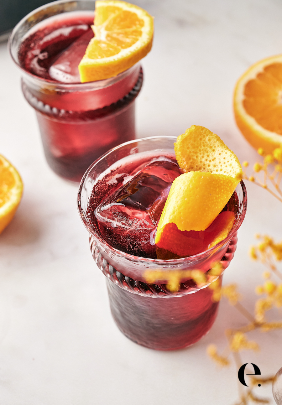 Two glasses of tinto de verano over ice, garnished with orange slices, on a white marble counter