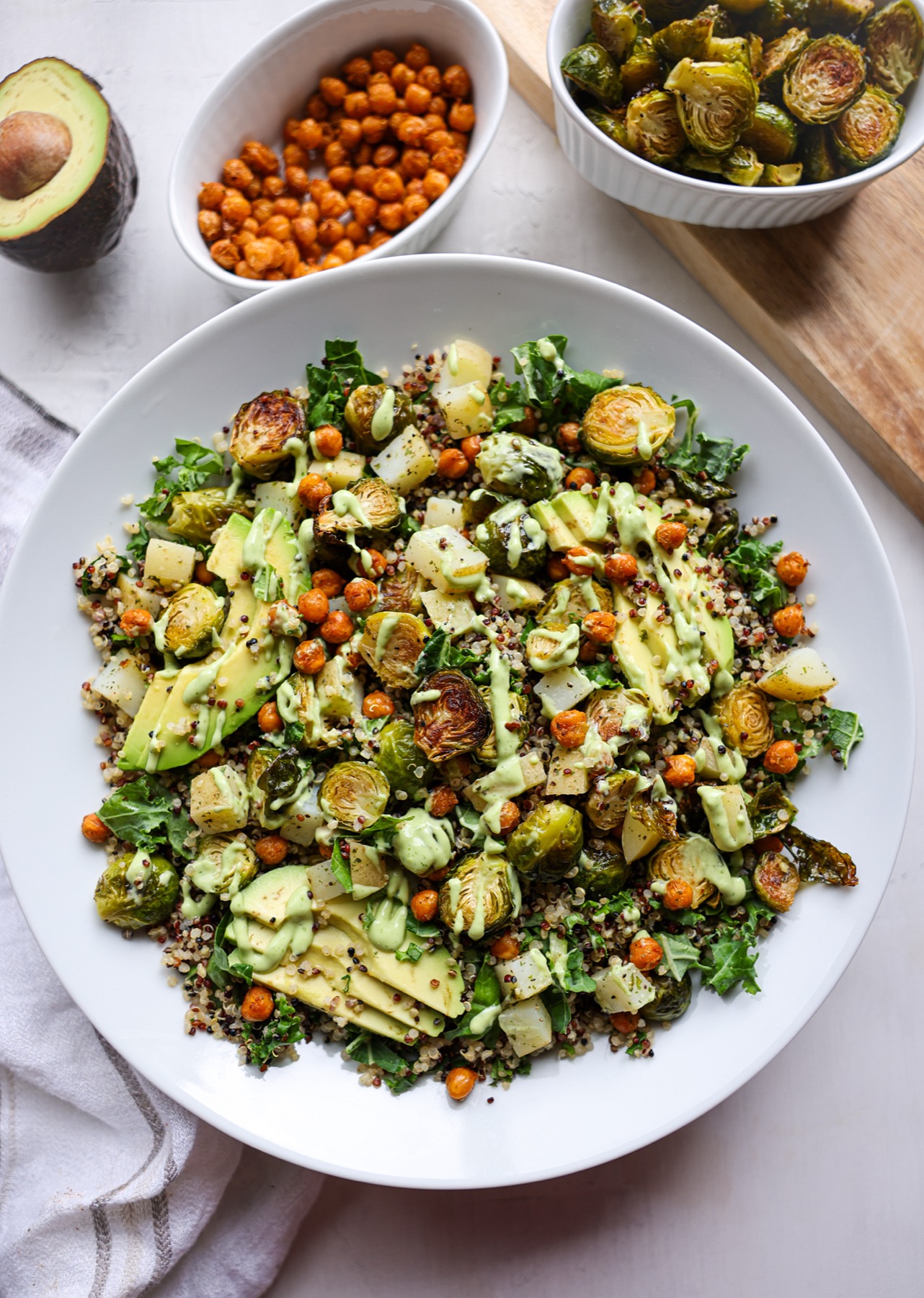 Brussels sprouts quinoa bowl with roasted Brussels sprouts, crispy chickpeas, potatoes, kale and sliced avocado drizzled with creamy avocado dressing