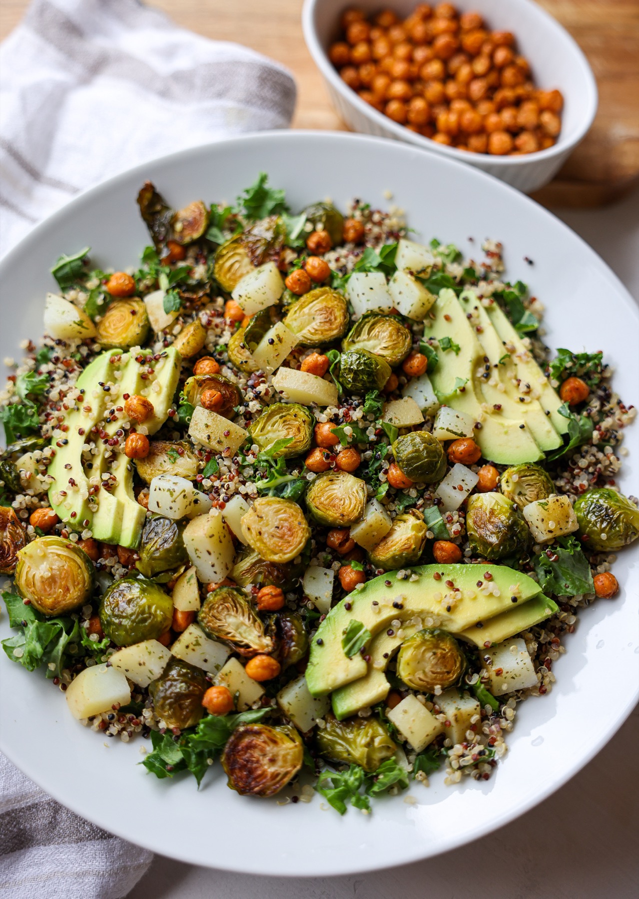 Quinoa bowl with roasted Brussels sprouts, crispy chickpeas, potatoes, kale and avocado, with a bowl of roasted chickpeas behind it