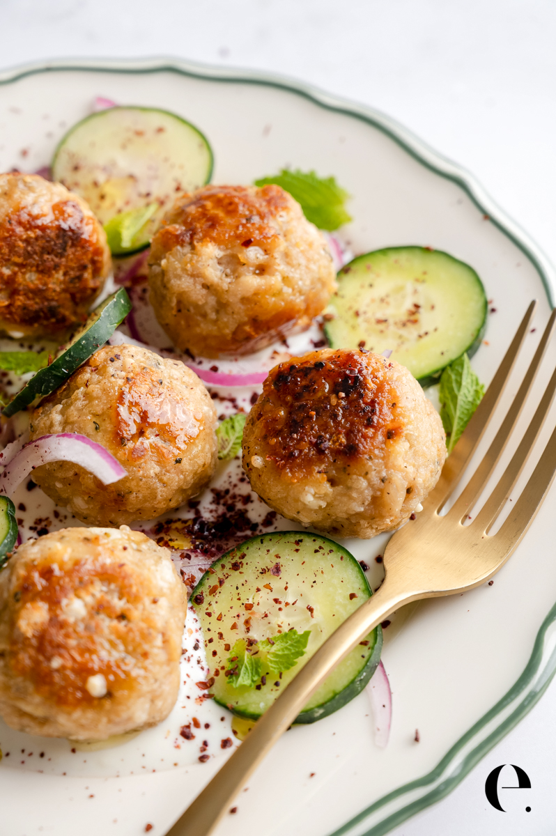 Juicy Greek chicken meatballs with feta served over garlic yogurt, cucumber slices, and pickled red onion closeup