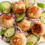 Greek chicken meatballs seared golden brown on garlic yogurt sauce with sliced cucumber, red onion, fresh mint, and sumac