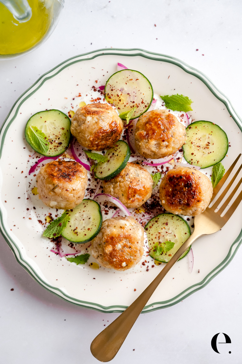 Easy Greek chicken meatballs on a platter with Greek yogurt sauce, cucumber, red onion, and herbs