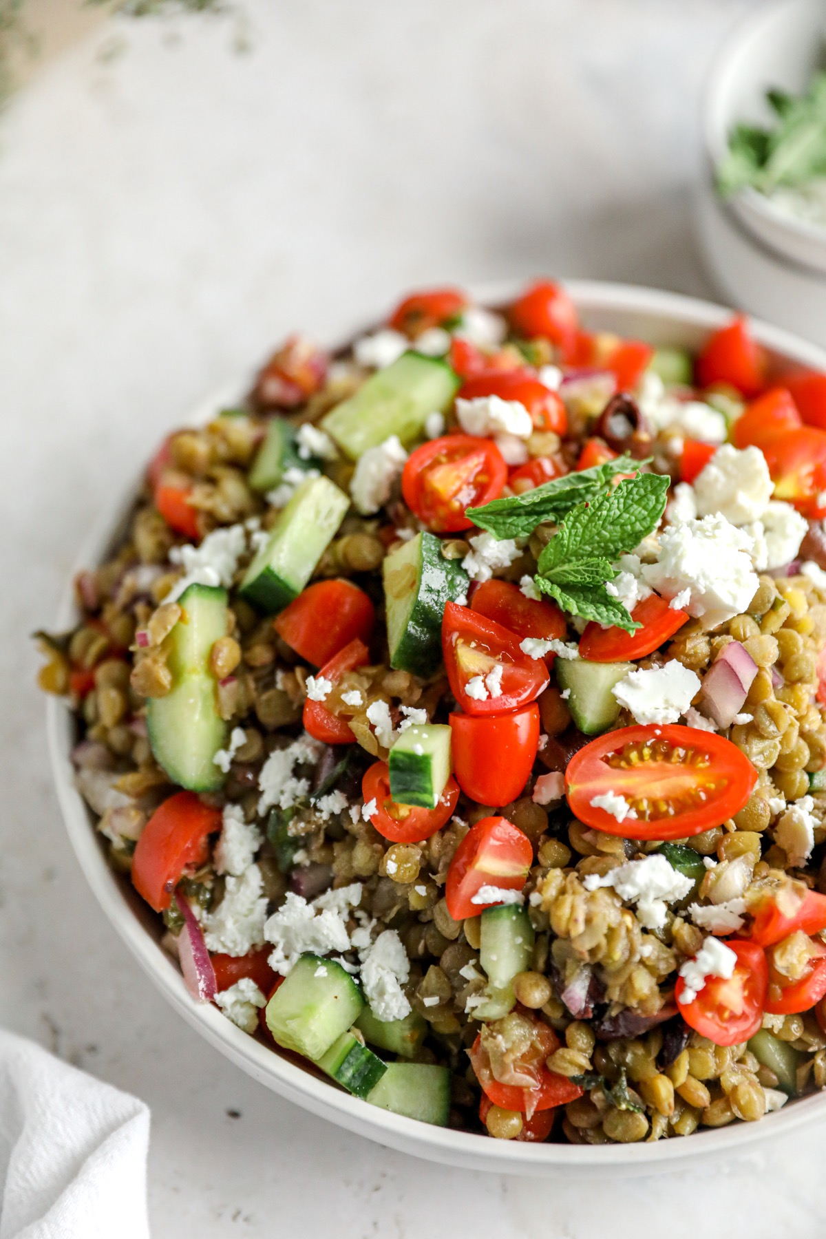 Green lentil salad with cherry tomatoes, cucumber, red onion, Kalamata olives, feta and fresh mint in a white bowl