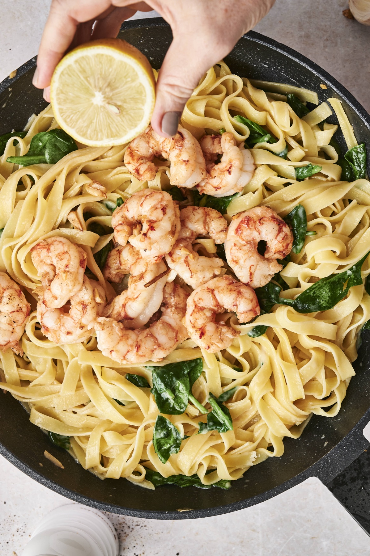 Squeezing fresh lemon over shrimp pasta with spinach in a skillet