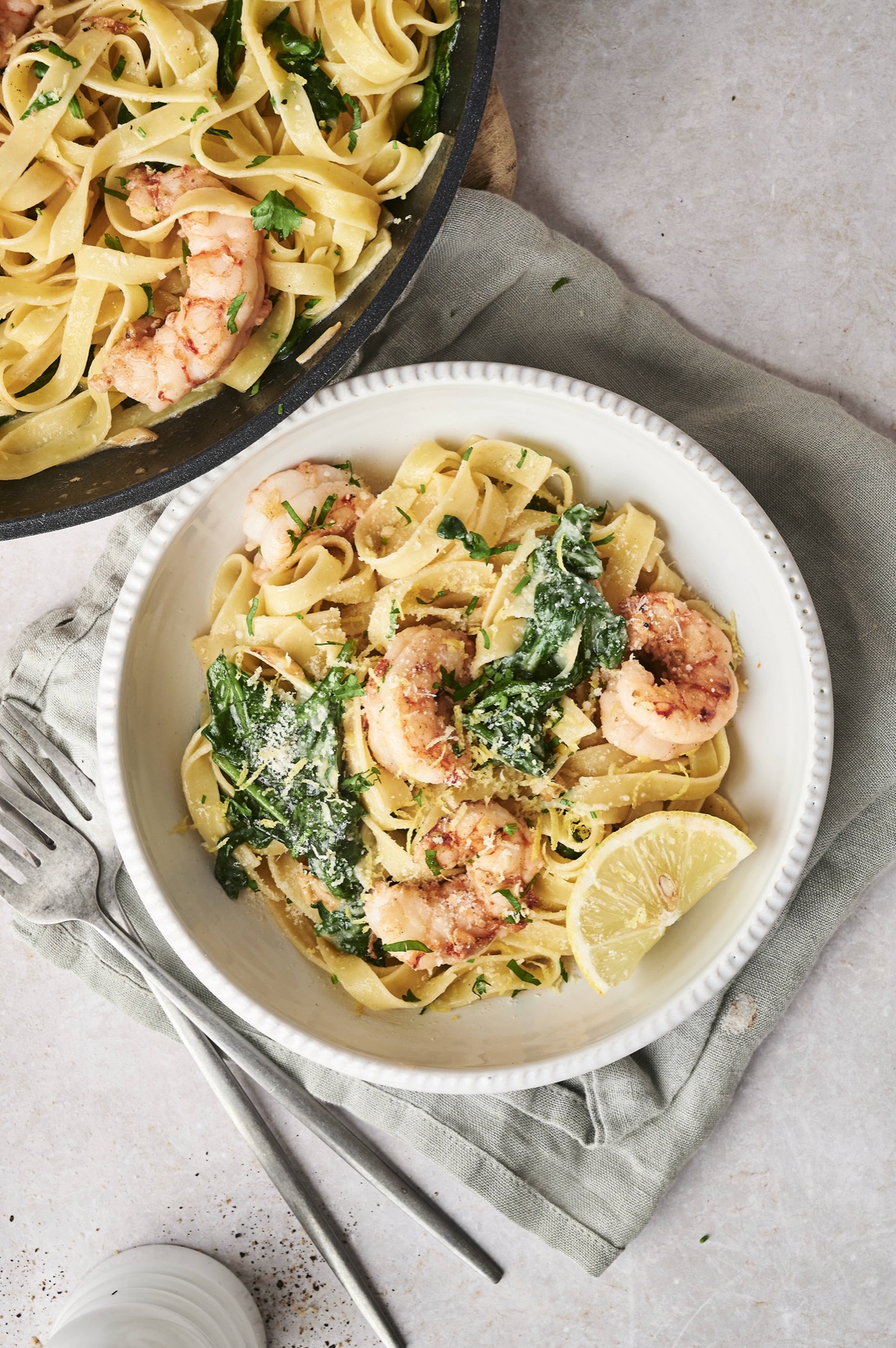 Lemon garlic shrimp pasta with spinach in a white bowl next to the skillet