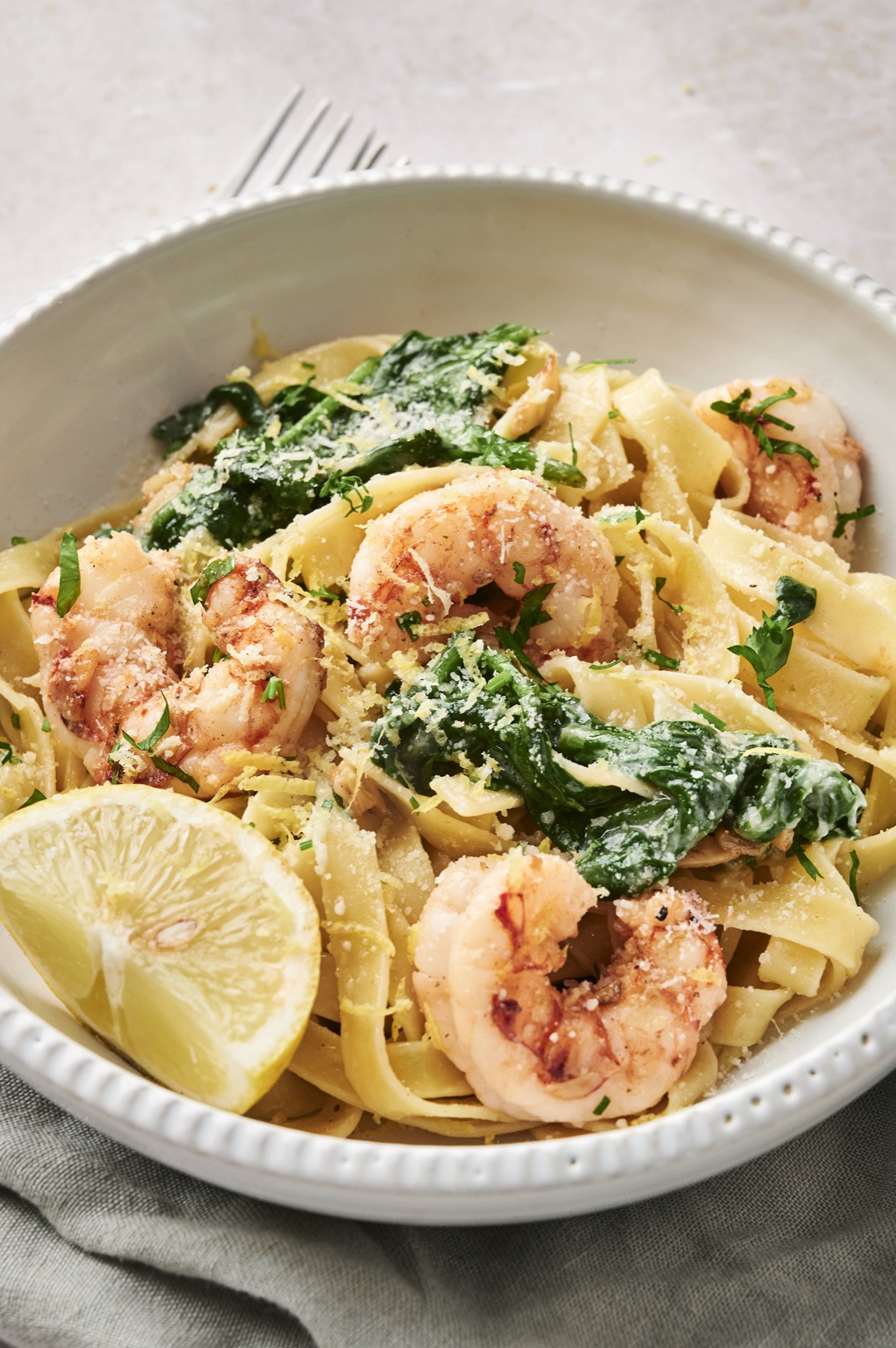 Close-up of lemon garlic shrimp pasta with spinach and a lemon wedge