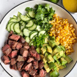 Steak salad with avocado and corn in a white bowl, with a fresh lime and a small dish of honey-lime dressing on the side