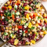 Overhead view of a vibrant dense bean salad with diced peppers, cucumber, Castelvetrano olives, and crumbled feta