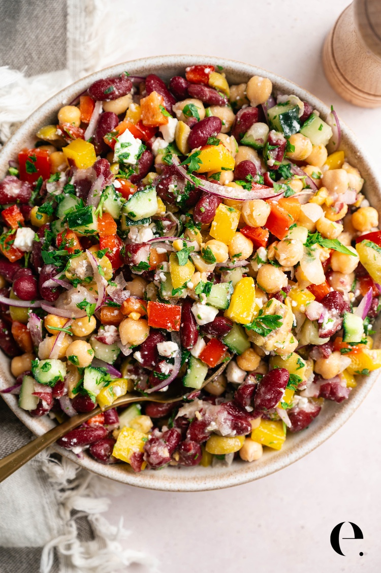 Overhead view of a vibrant dense bean salad with diced peppers, cucumber, Castelvetrano olives, and crumbled feta