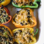 Quinoa stuffed peppers baked in a white dish, filled with quinoa, black beans and melted cheese