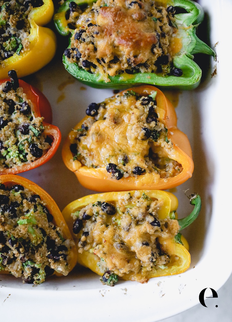Quinoa stuffed peppers baked in a white dish, filled with quinoa, black beans and melted cheese