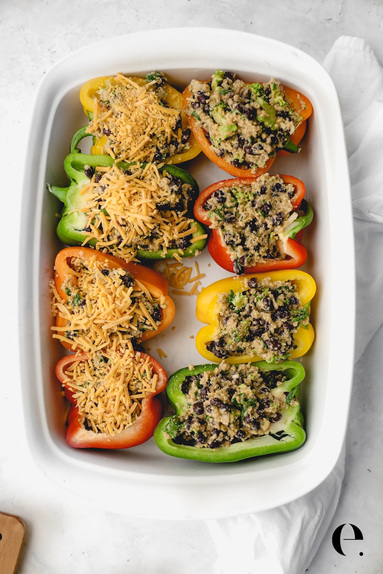 Bell pepper halves stuffed with quinoa and black bean filling and topped with shredded cheese before baking