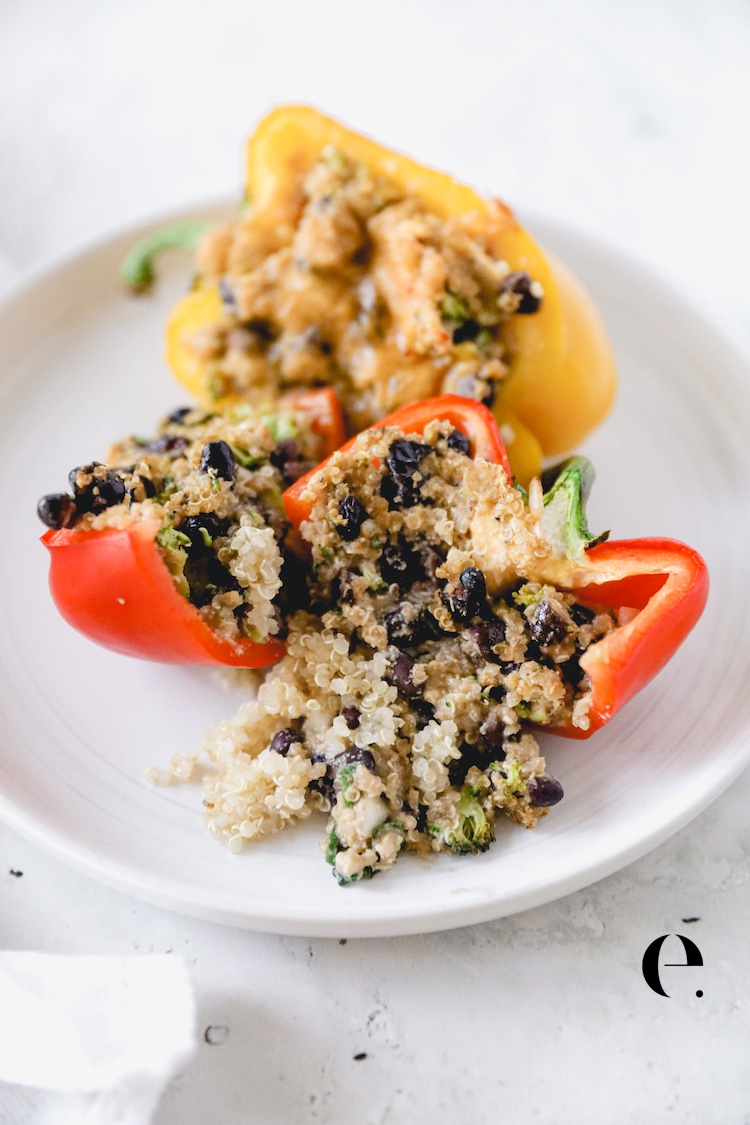 Two quinoa stuffed pepper halves with black beans and cheese on a white plate