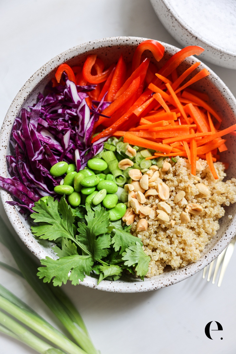 Thai peanut quinoa salad ingredients in a bowl: quinoa, red cabbage, carrots, bell pepper, edamame, cilantro and peanuts