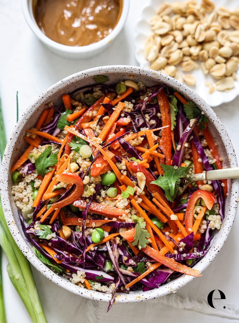 Bowl of Thai peanut quinoa salad with peanut sauce and chopped peanuts on the side